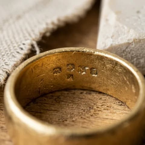 The hallmark or tag, close up. Gold rings, a chain and diamond studs beside an emerald ring in a red velvet box.