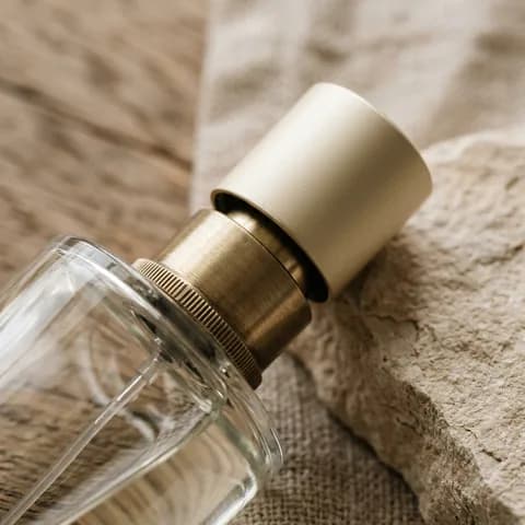 The sprayer and the cap. Perfume bottles, lipstick, mascara, a compact and a brush on a peach background.